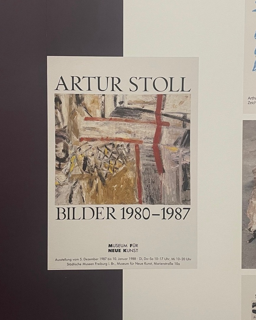 Dieser Alternativtext wurde KI-generiert: Schwarz-weißes Foto einer Plakatwand. Das Plakat zeigt ein abstraktes Gemälde und Informationen zu einer Ausstellung.