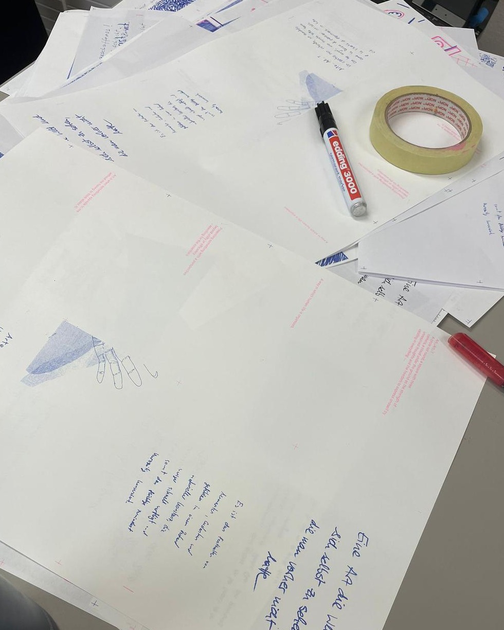 Dieser Alternativtext wurde KI-generiert: Ein Schwarz-Weiß-Foto zeigt mehrere beschriftete Blätter Papier, Schreibutensilien und Klebeband auf einer Oberfläche. Die Papiere enthalten handschriftliche Notizen und Skizzen.