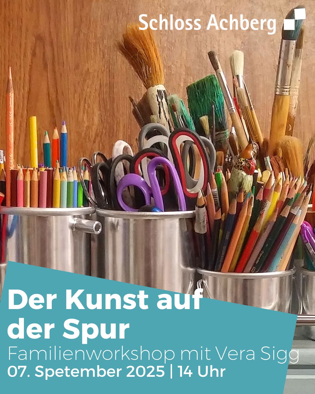 Ein Arrangement aus Schreibgeräten wie Pinseln und Stiften steht in einem Metallbehälter. Im Vordergrund befindet sich eine Texttafel mit Informationen zu einem Kunstworkshop.