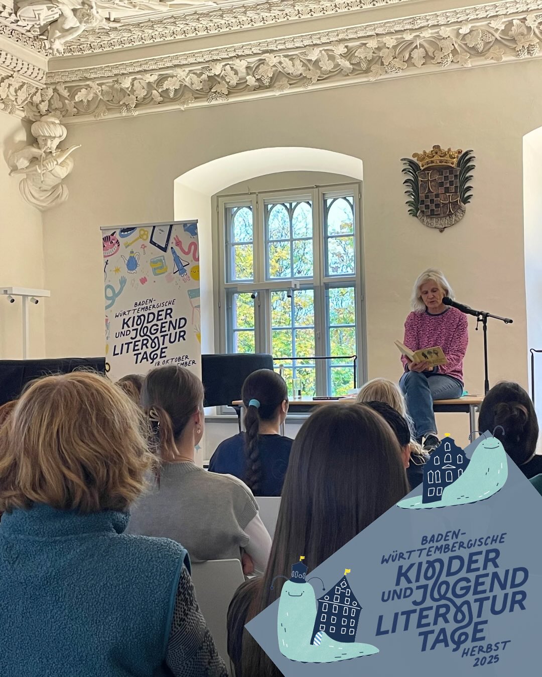 Dieser Alternativtext wurde KI-generiert: Eine Person liest aus einem Buch vor einer Gruppe von Zuhörer*innen, die auf Kissen sitzen. Im Hintergrund befindet sich eine Tür und Wanddekorationen.