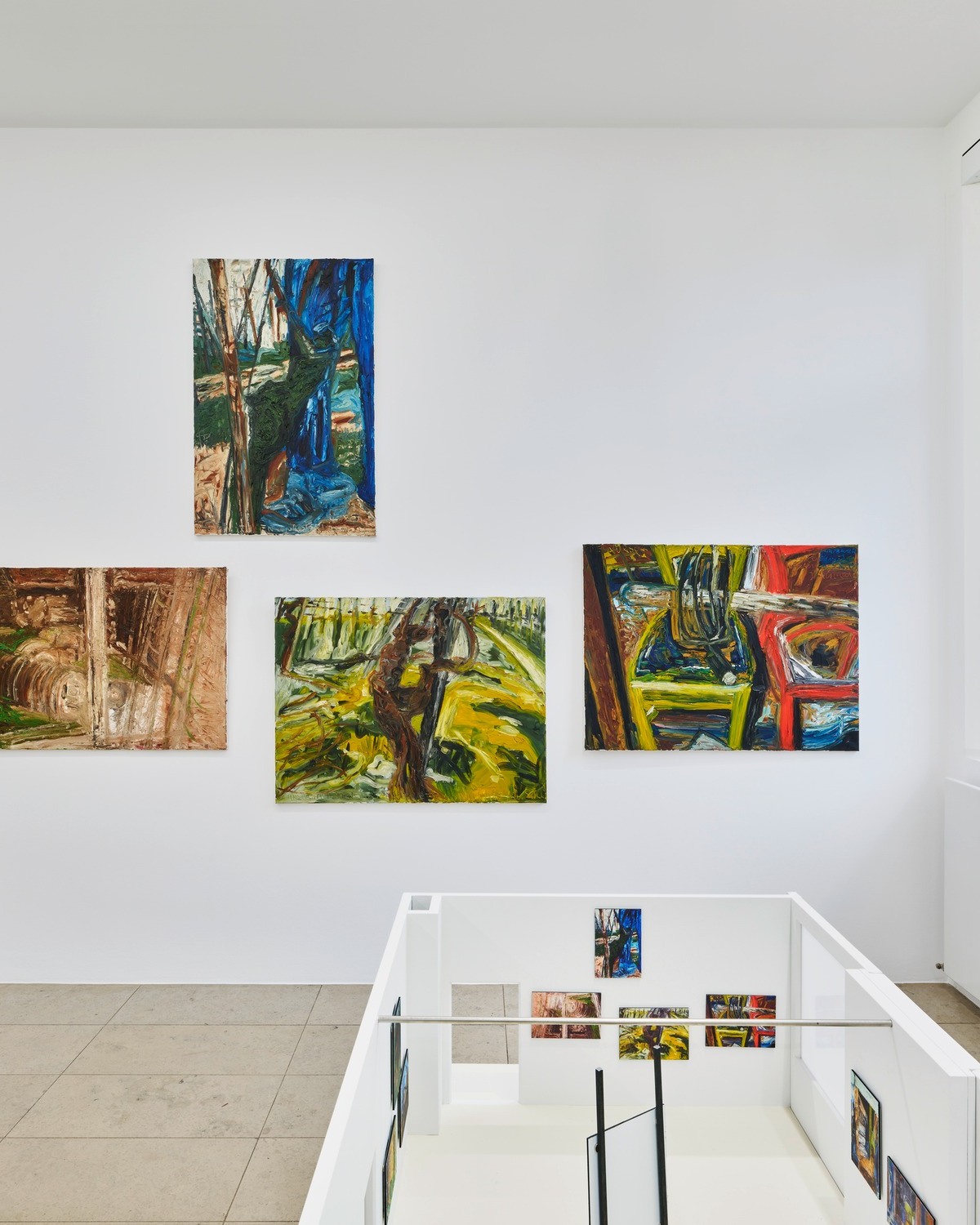 Dieser Alternativtext wurde KI-generiert: Mehrere farbenfrohe Gemälde hängen an einer weißen Wand. Im Vordergrund ist eine weiße Balustrade zu sehen, unter der sich weitere Bilder befinden.
