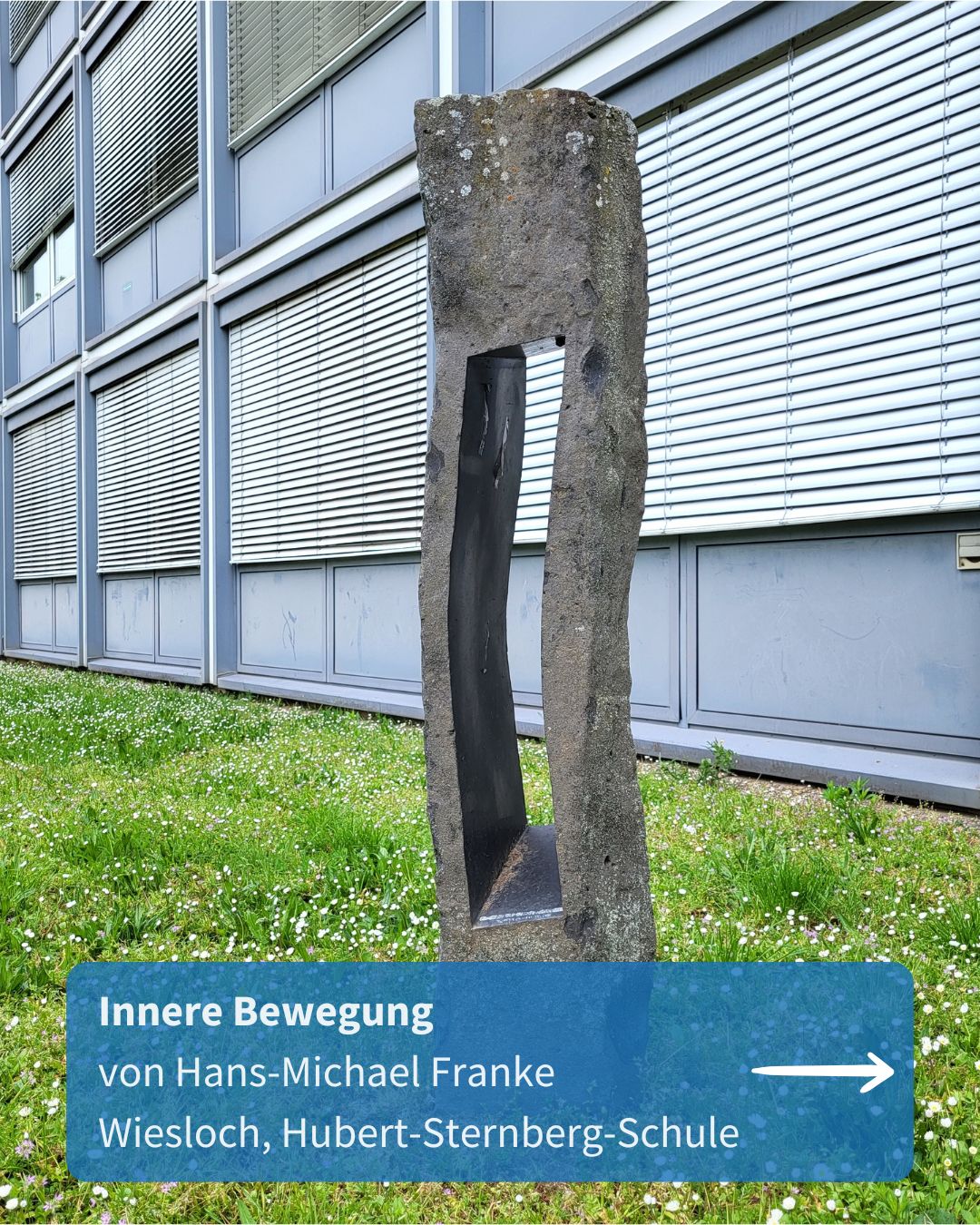 Eine hohe Steinskulptur mit einem rechteckigen Ausschnitt steht auf einer Wiese vor einem Gebäude mit grauer Fassade. Ein blauer Textkasten unten enthält die Aufschrift „Innere Bewegung von Hans-Michael Franke Wiesloch, Hubert-Sternberg-Schule“ und einen weißen Pfeil nach rechts. (KI-Alternativtext)