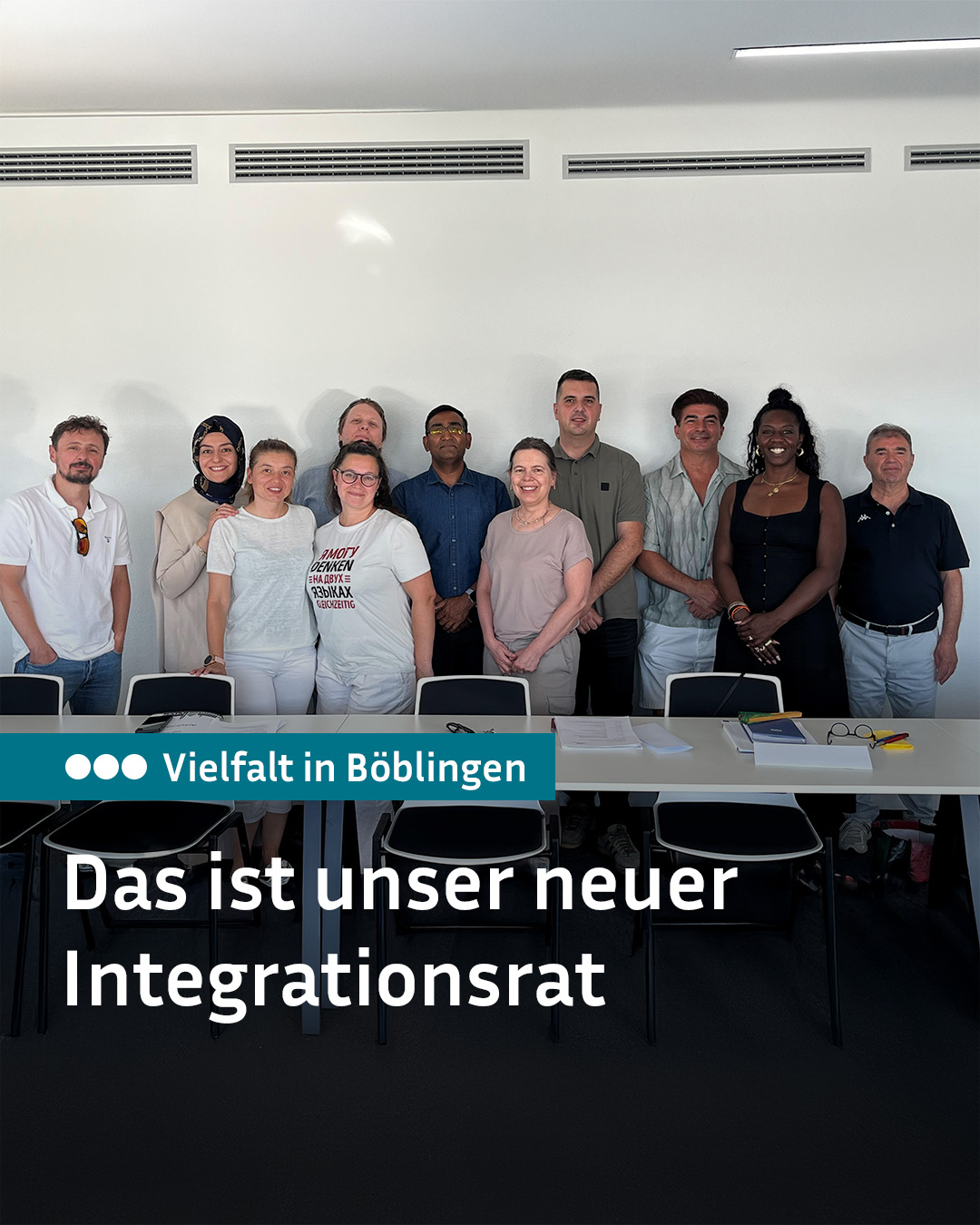 Zehn Personen stehen lächelnd hinter einem Tisch in einem hellen Raum. Ein blaues Banner trägt die Aufschrift "Vielfalt in Böblingen" und darunter steht in großen weißen Buchstaben "Das ist unser neuer Integrationsrat". (KI-Alternativtext)