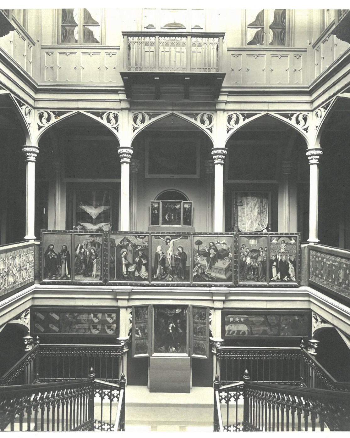 Dieser Alternativtext wurde KI-generiert: Schwarz-weißes Foto einer Innenansicht mit Arkaden und einer Treppe. An den Wänden sind Gemälde zu sehen.