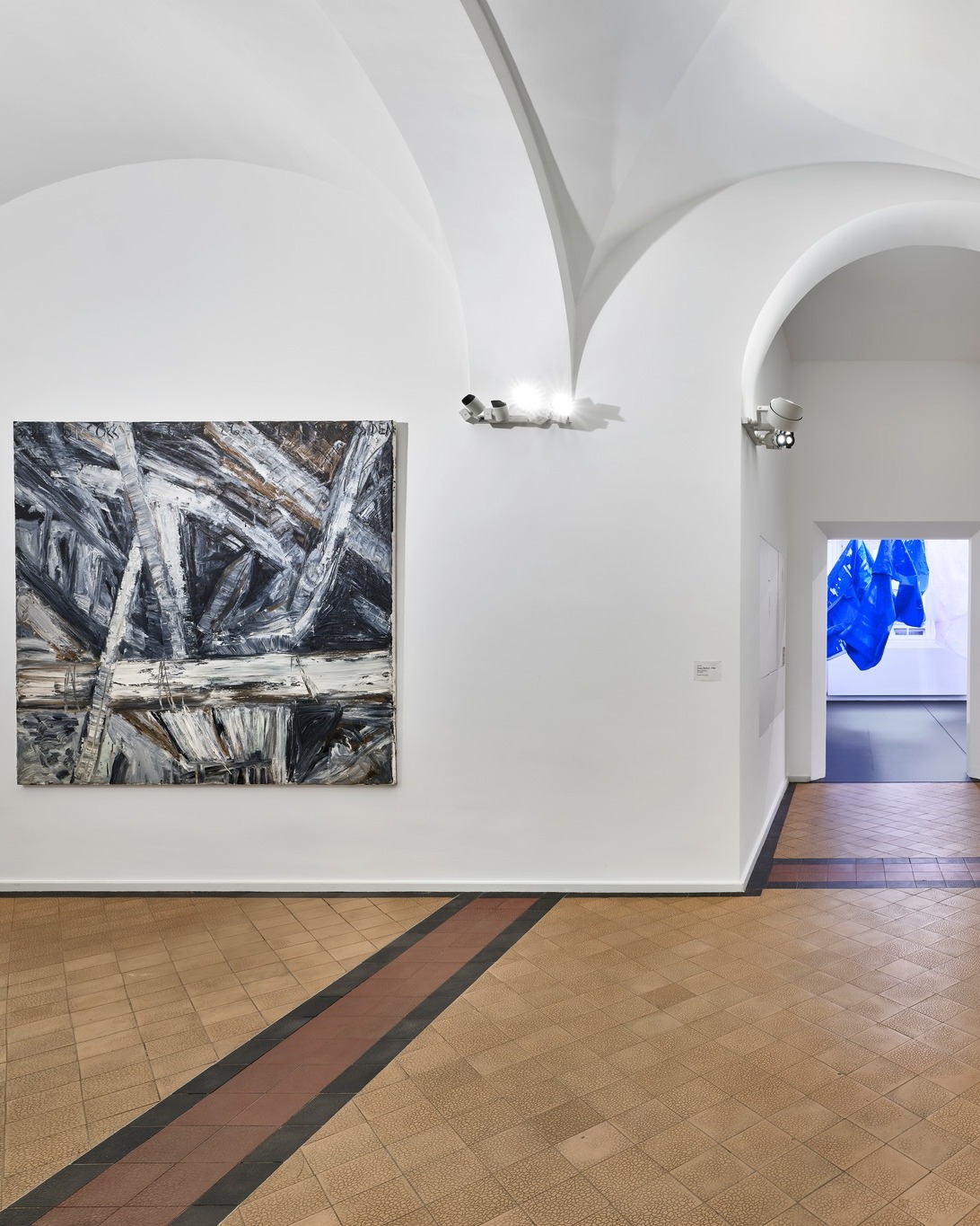 Dieser Alternativtext wurde KI-generiert: Ein Innenraum mit gewölbter Decke zeigt Kunstwerke an den Wänden. Im Vordergrund ist ein gemusterter Boden zu sehen.