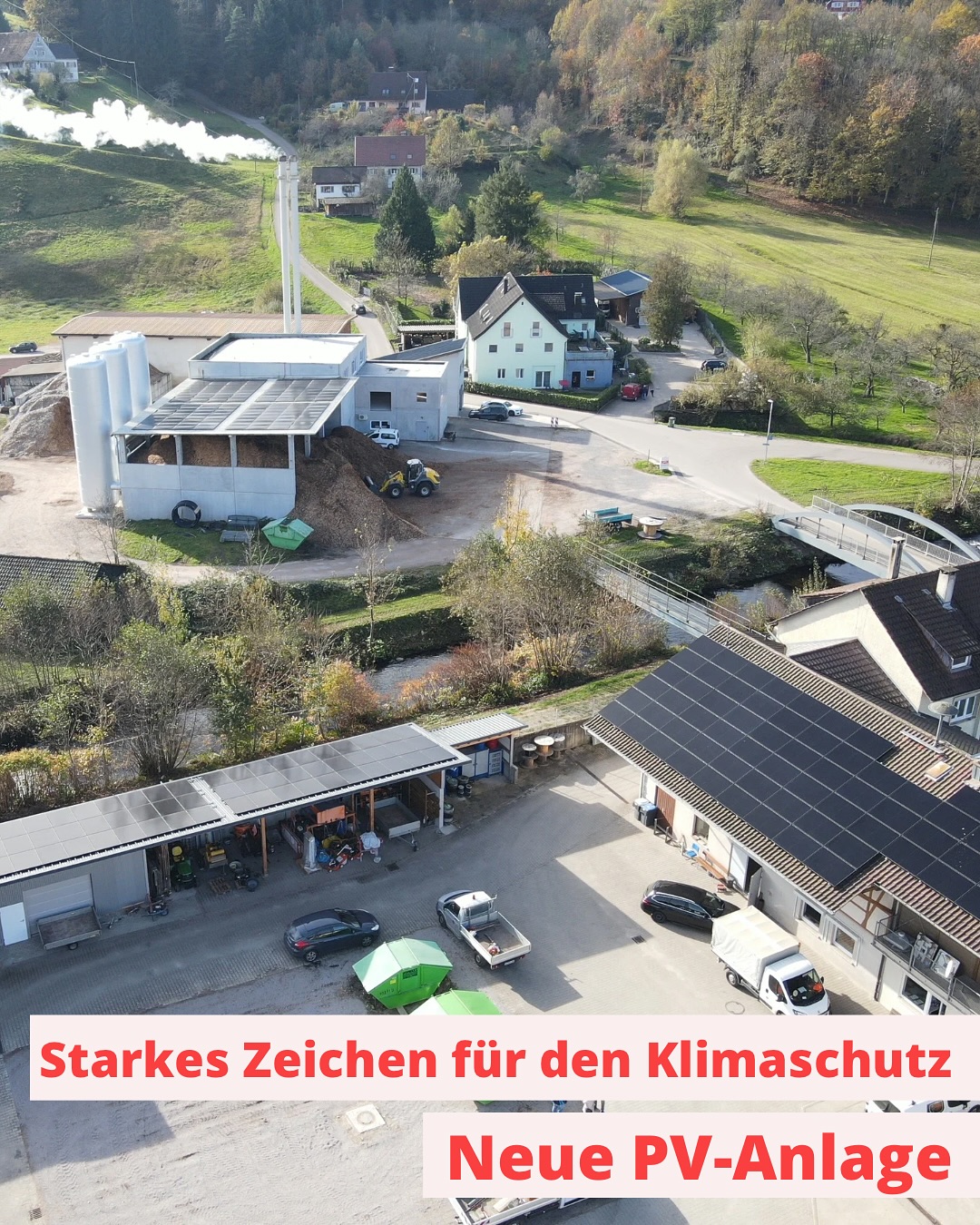 Eine Vogelperspektive zeigt ein Fabrikgebäude, Häuser und Straßen in einer ländlichen Umgebung. Das Dach des Gebäudes ist mit Solarpaneelen ausgestattet.