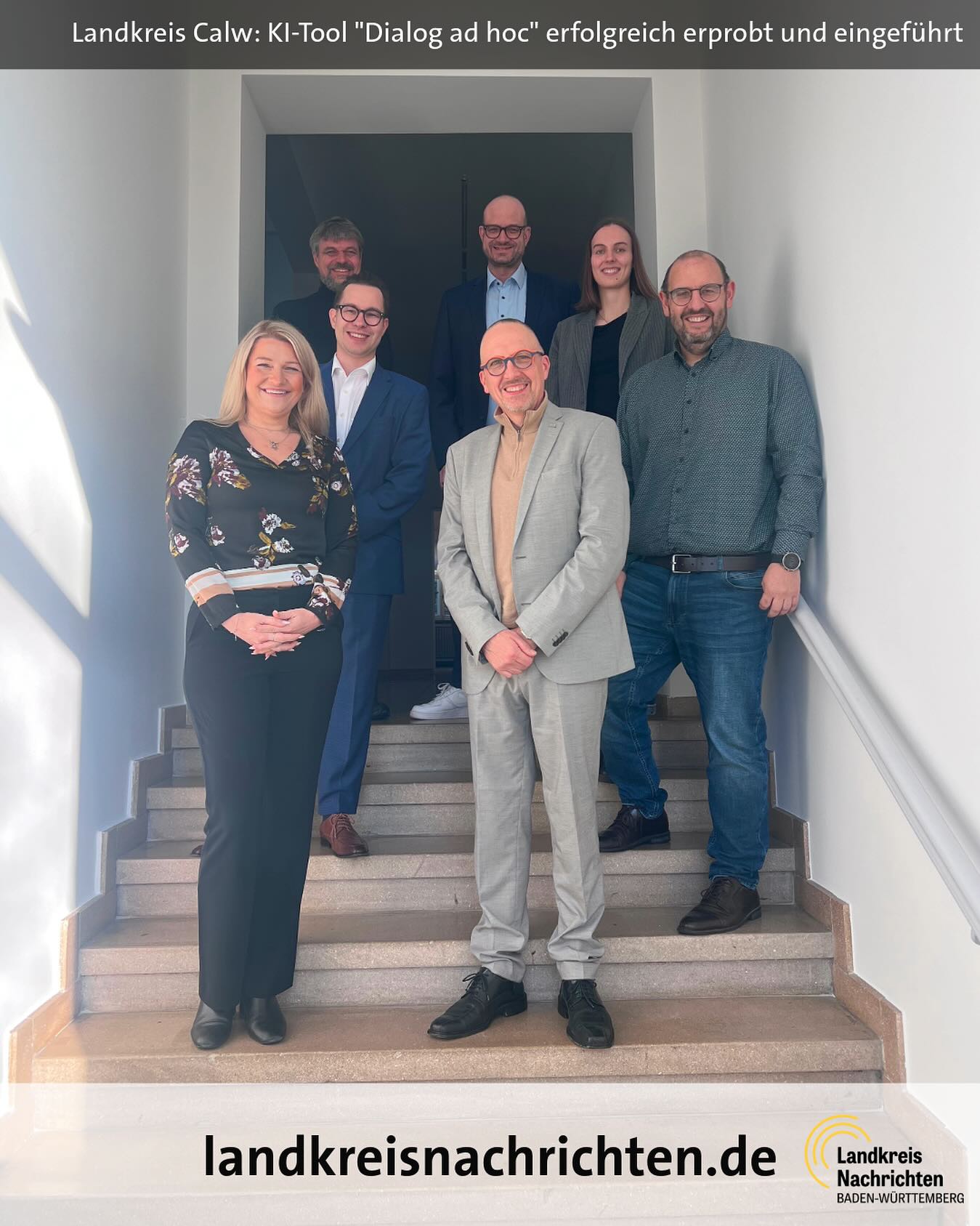 Dieser Alternativtext wurde KI-generiert: Eine Gruppe von Personen steht auf einer Treppe vor einem Gebäude. Im unteren Bildbereich befindet sich ein Logo und eine Internetadresse.