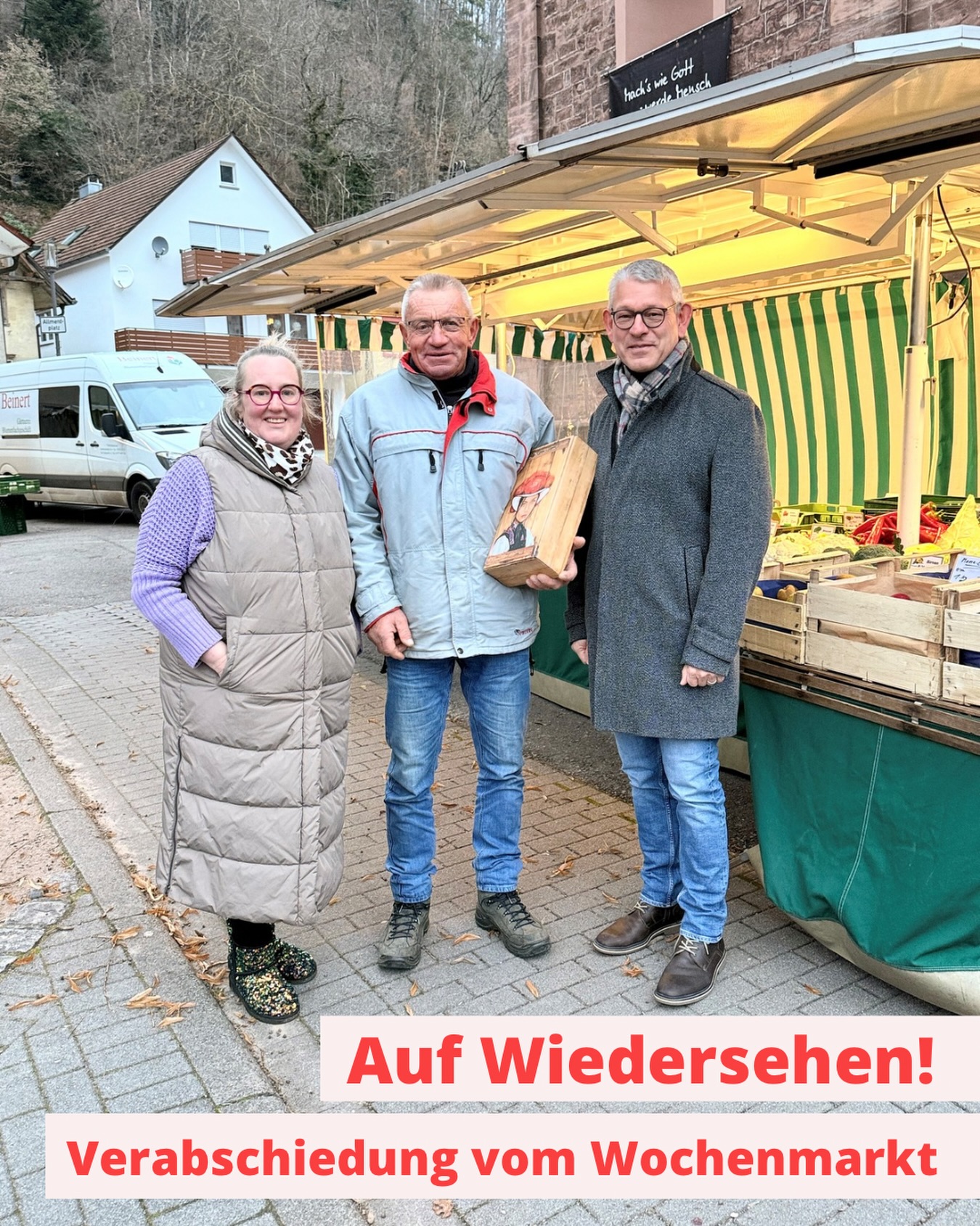 Dieser Alternativtext wurde KI-generiert: Drei Personen stehen lächelnd vor einem Marktstand und einem Lieferwagen im Freien. Im Hintergrund ist ein Schild mit der Aufschrift „Auf Wiedersehen“ zu sehen.