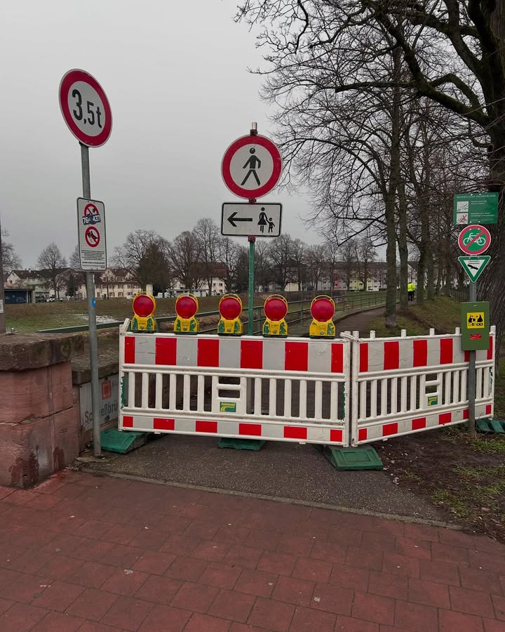 Dieser Alternativtext wurde KI-generiert: Ein Straßenverkehrsschild und ein Fußgängerschild sind zu sehen. Im Vordergrund befindet sich eine Absperrung mit rotem und weißem Streifenmuster.