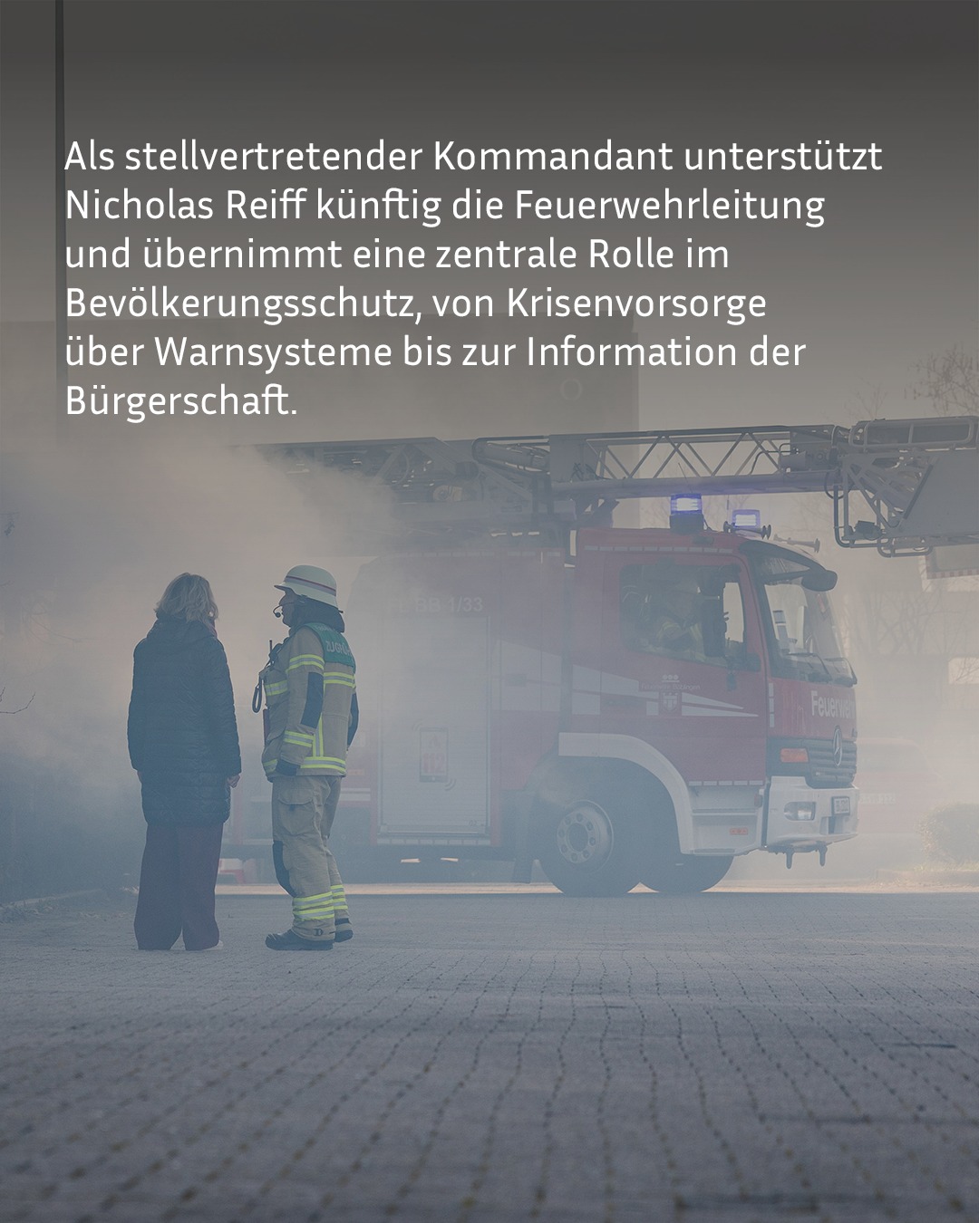 Eine Person in Feuerwehruniform steht neben einer Person in Zivilkleidung vor einem roten Löschfahrzeug mit ausfahrbarem Gerüst und leichtem Rauch im Hintergrund. Ein Textfeld im oberen Bildbereich lautet: „Als stellvertretender Kommandant unterstützt Nicholas Reiff künftig die Feuerwehrleitung und übernimmt eine zentrale Rolle im Bevölkerungsschutz, von Krisenvorsorge über Warnsysteme bis zur Information der Bürgerschaft.“ (KI-Alternativtext)