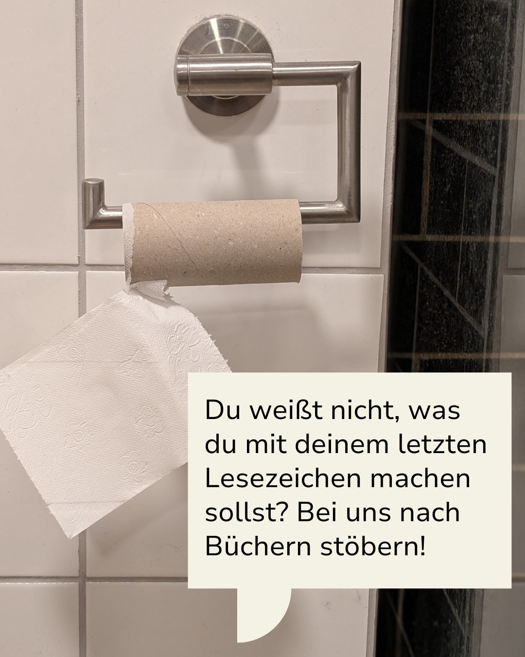 Dieser Alternativtext wurde KI-generiert: Ein Toilettenpapierhalter an einer gekachelten Wand mit einer fast leeren Rolle Papier. Ein Schild mit Text ist darunter angebracht.