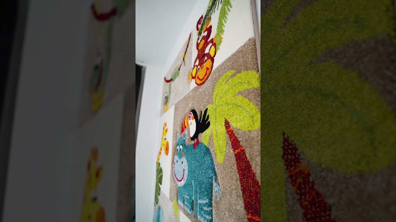 Dieser Alternativtext wurde KI-generiert: Ein Teppich mit Tiermotiven hängt an einer Wand. Die Motive zeigen verschiedene Tiere und Pflanzen in bunten Farben.