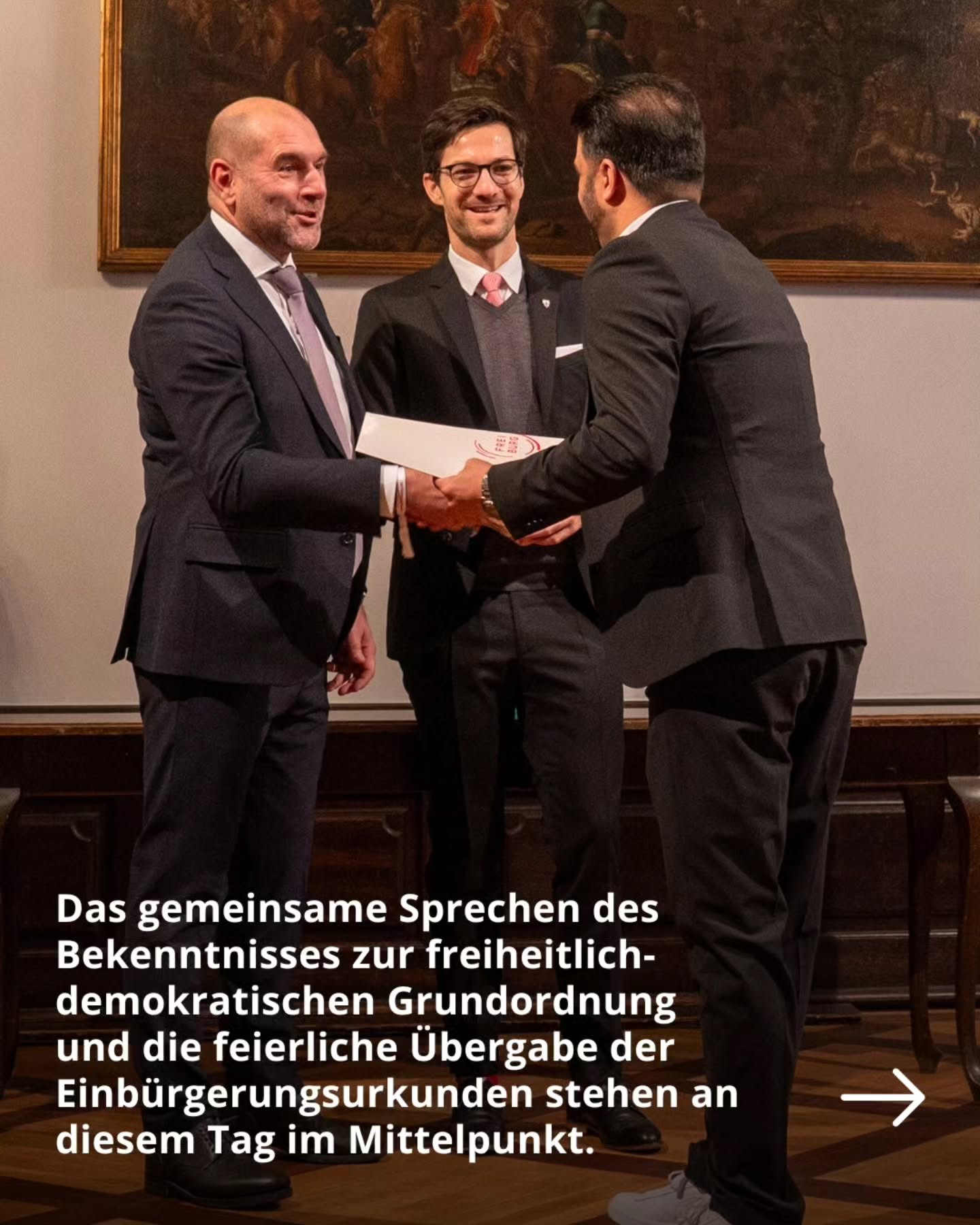 Dieser Alternativtext wurde KI-generiert: Eine Aufnahme zeigt Personen in dunkler Kleidung in Innenräumen bei einer feierlichen Zeremonie. Ein Dokument wird überreicht, während andere zusehen.