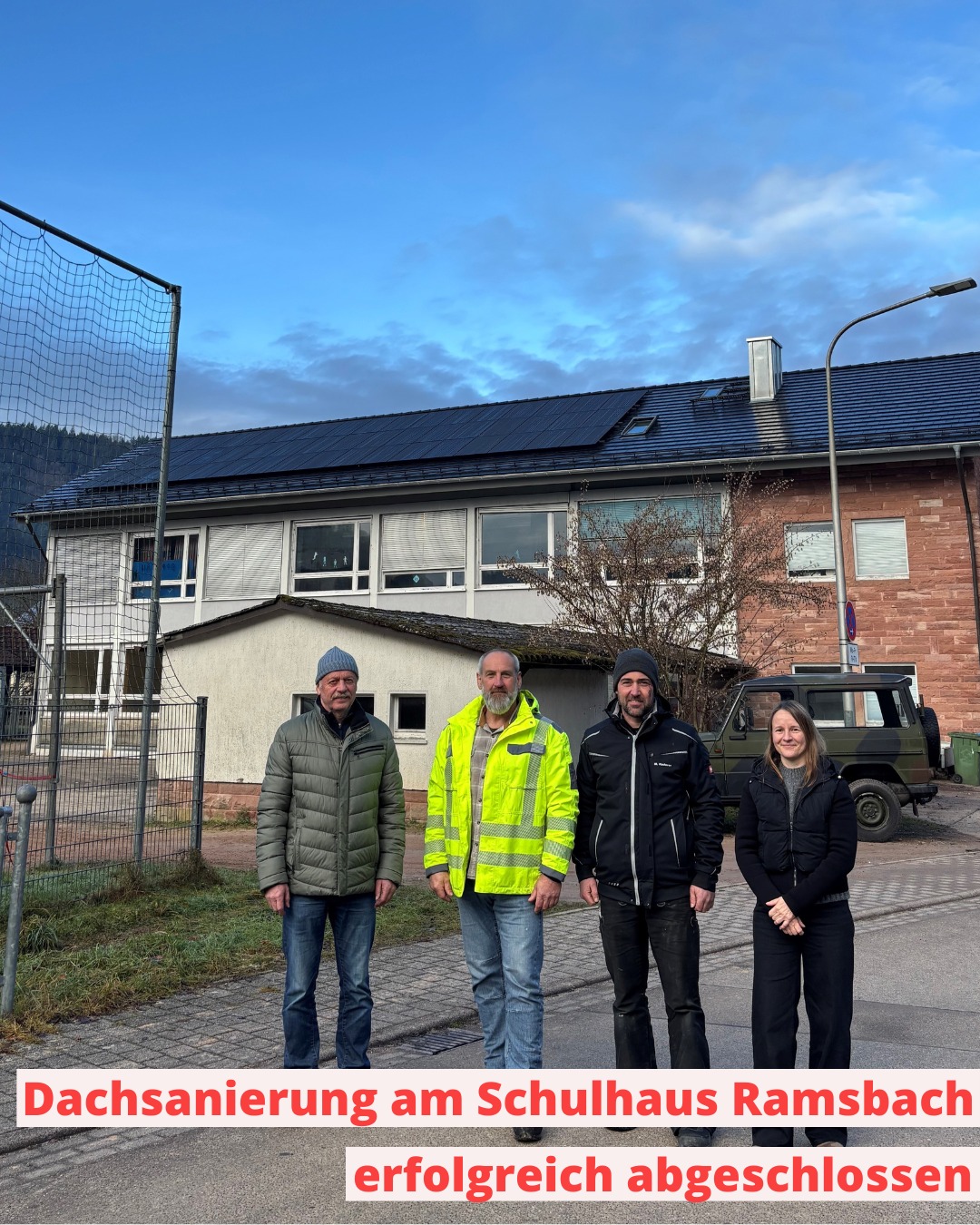 Dieser Alternativtext wurde KI-generiert: Ein Gebäude mit einem neuen Dach ist im Hintergrund zu sehen. Mehrere Personen stehen davor und schauen in die Kamera.