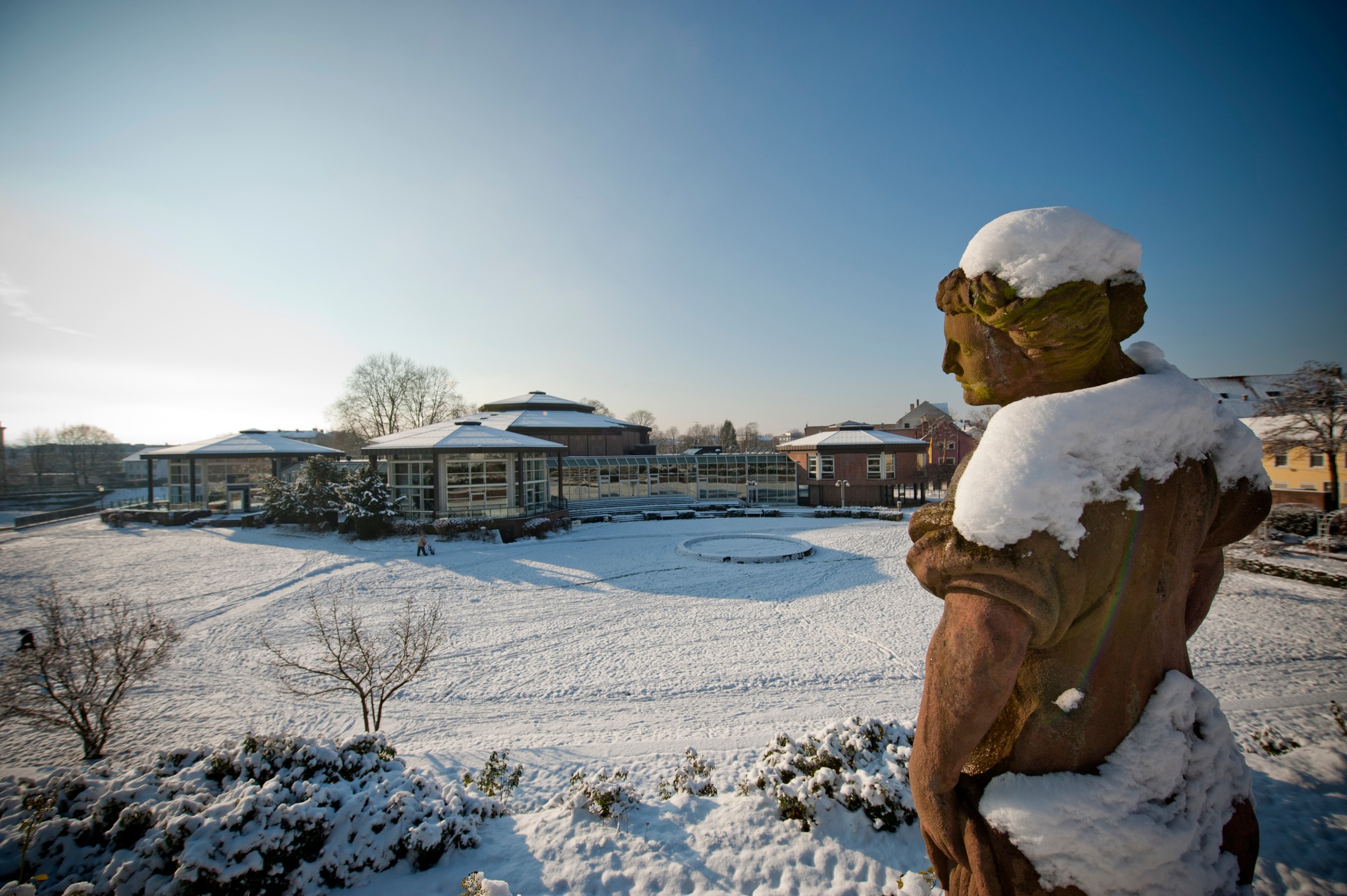 Dieser Alternativtext wurde KI-generiert: Eine verschneite Landschaft mit Gebäuden im Hintergrund. Im Vordergrund befindet sich eine teilweise schneebedeckte Skulptur.