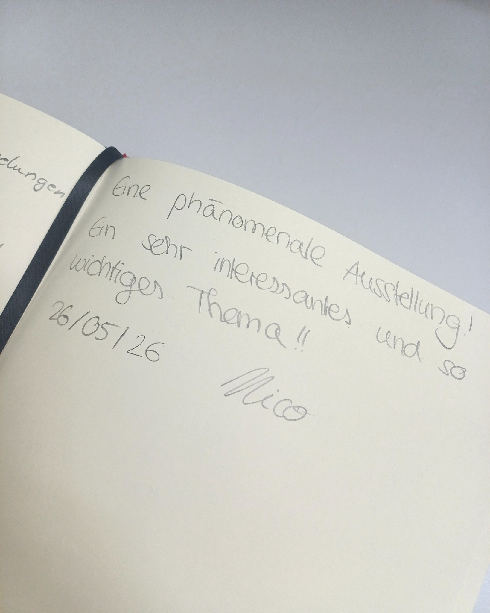 Eine Seite eines Notizbuchs mit handschriftlichem Text. Der Eintrag lautet: "Eine phänomenale Ausstellung! Ein sehr interessantes und so wichtiges Thema!! 26/05/26 Mico". (KI-Alternativtext)
