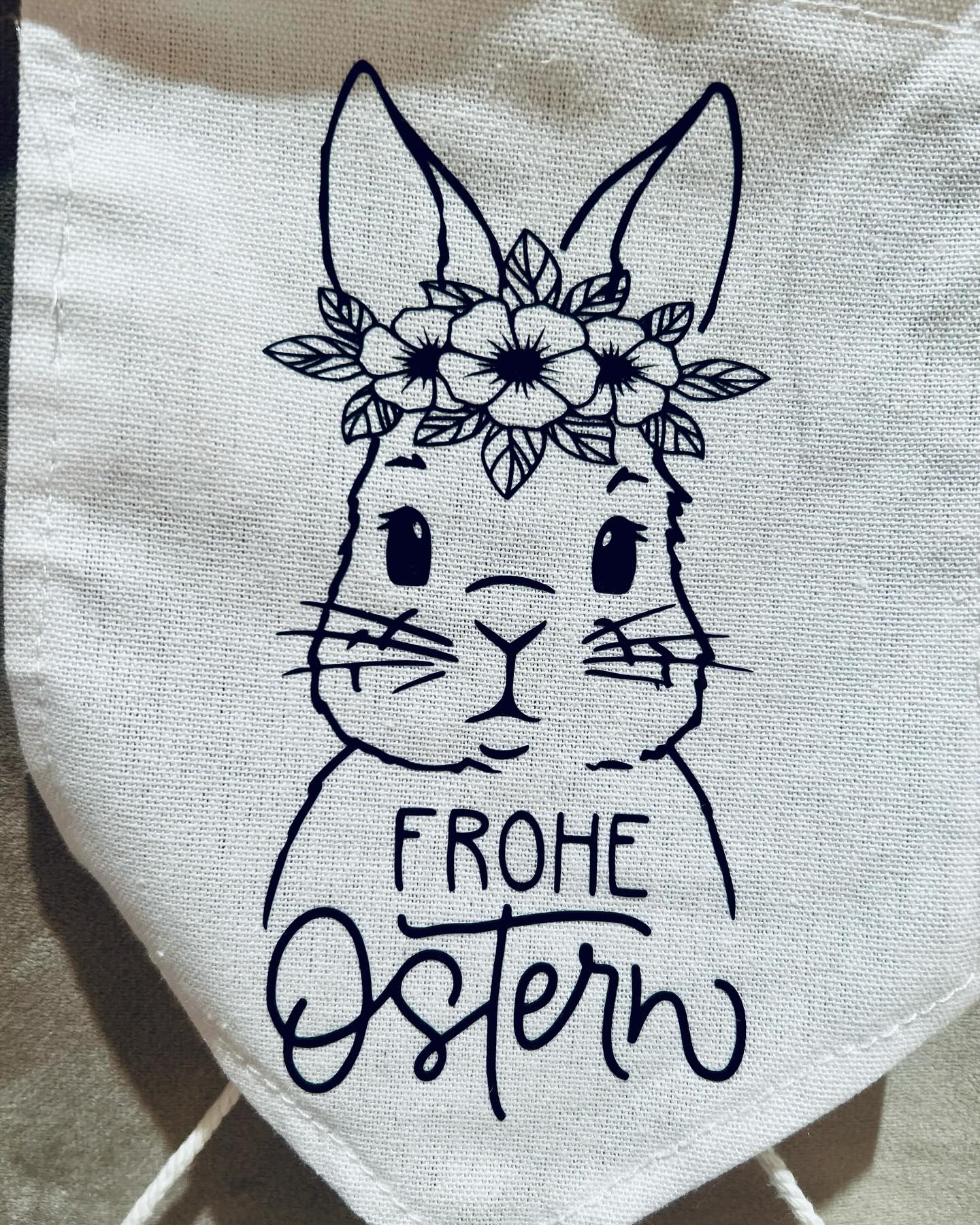 Ein Stoffbanner mit einer Zeichnung eines Hasen mit einem Blumenkranz auf dem Kopf und der Aufschrift "Frohe Ostern".