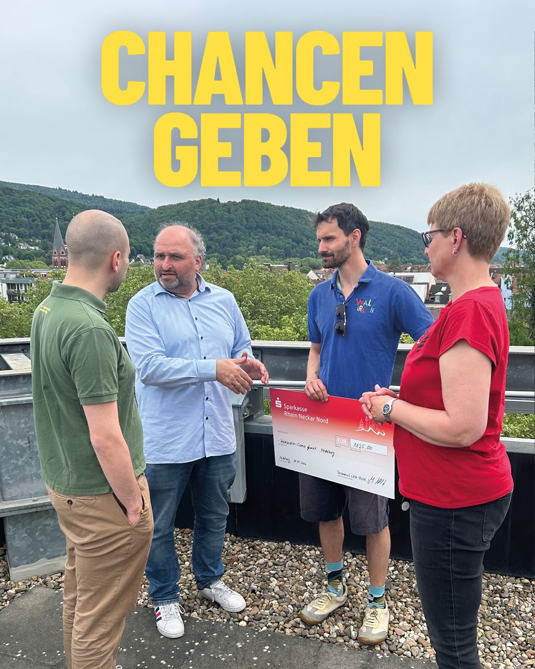 Vier Personen stehen im Freien auf einem Dach, eine hält einen großen Spendenscheck der Sparkasse Rhein Neckar Nord über 425 Euro. Im Hintergrund sind Hügel und Gebäude zu sehen, oben im Bild steht in gelben Großbuchstaben „CHANCEN GEBEN“. (KI-Alternativtext)