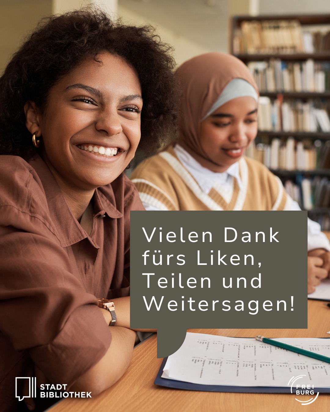 Zwei Personen sitzen an einem Tisch in einer Bibliothek, eine lächelt in die Kamera, die andere blickt auf ein Dokument. Ein Textfeld mit „Vielen Dank fürs Liken, Teilen und Weitersagen!“ ist überlagert, unten links das Logo „Stadt Bibliothek“, rechts unten „Freiburg“. (KI-Alternativtext)