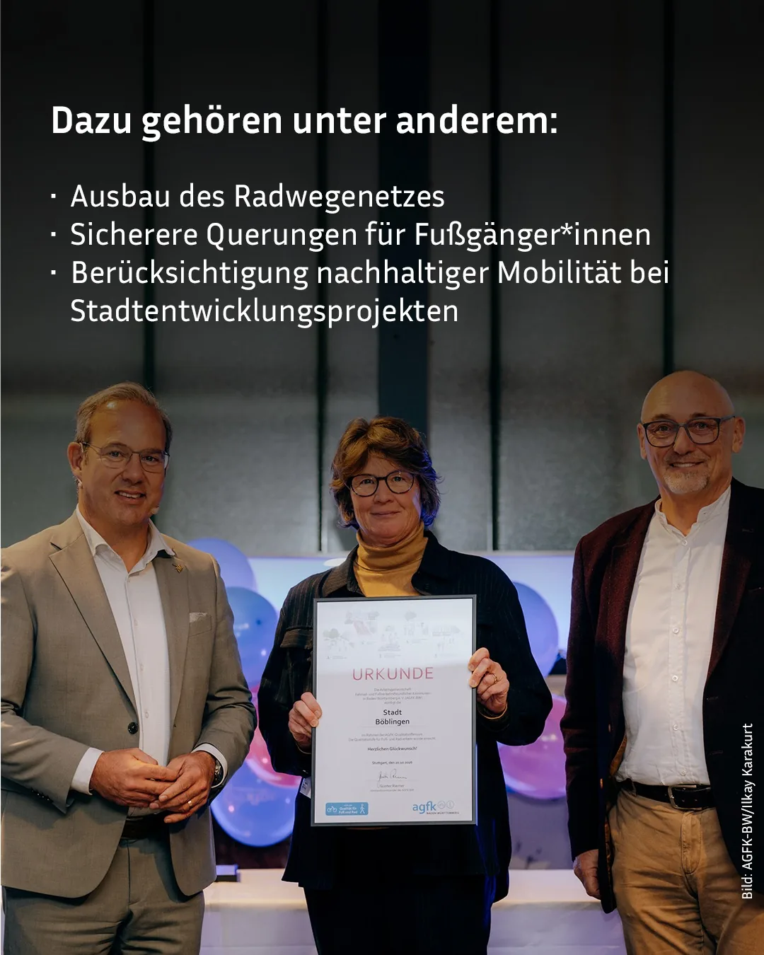 Drei Personen stehen nebeneinander vor einem Hintergrund mit blauen Luftballons. Die mittlere Person hält eine Urkunde der Stadt Böblingen mit dem Logo "agfk" hoch. Darüber steht weißer Text: "Dazu gehören unter anderem: Ausbau des Radwegenetzes, sicherere Querungen für Fußgänger*innen und Berücksichtigung nachhaltiger Mobilität bei Stadtentwicklungsprojekten." (KI-Alternativtext)