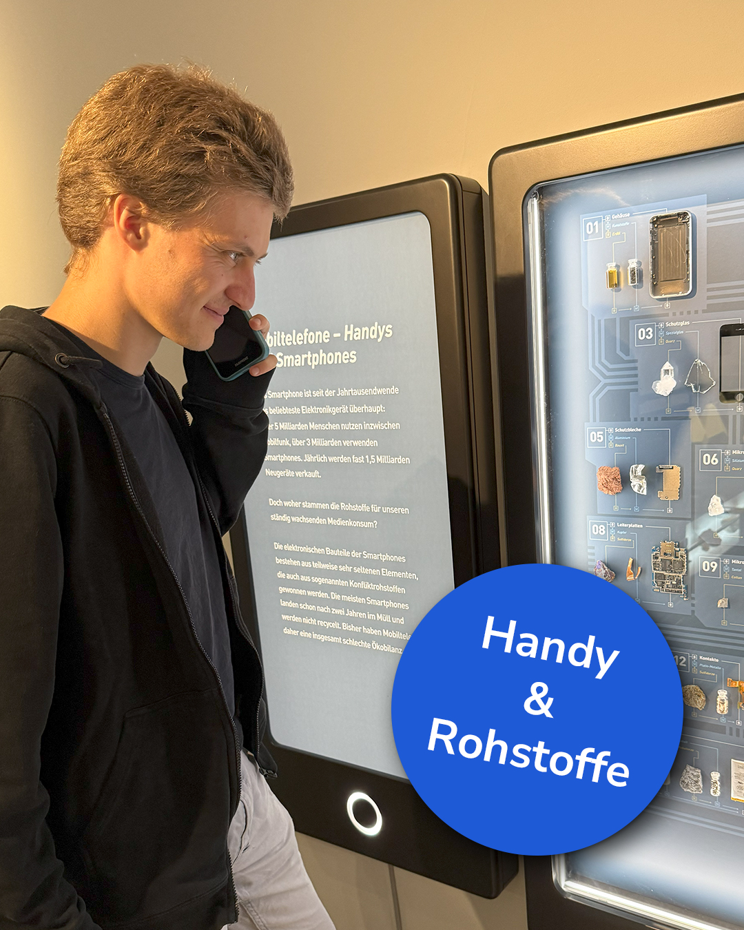 Dieser Alternativtext wurde KI-generiert: Eine Person steht vor einem Ausstellungsstück mit Informationen über Smartphones und deren Rohstoffe. Das Bild ist farbig und zeigt eine informative Ausstellungstafel.
