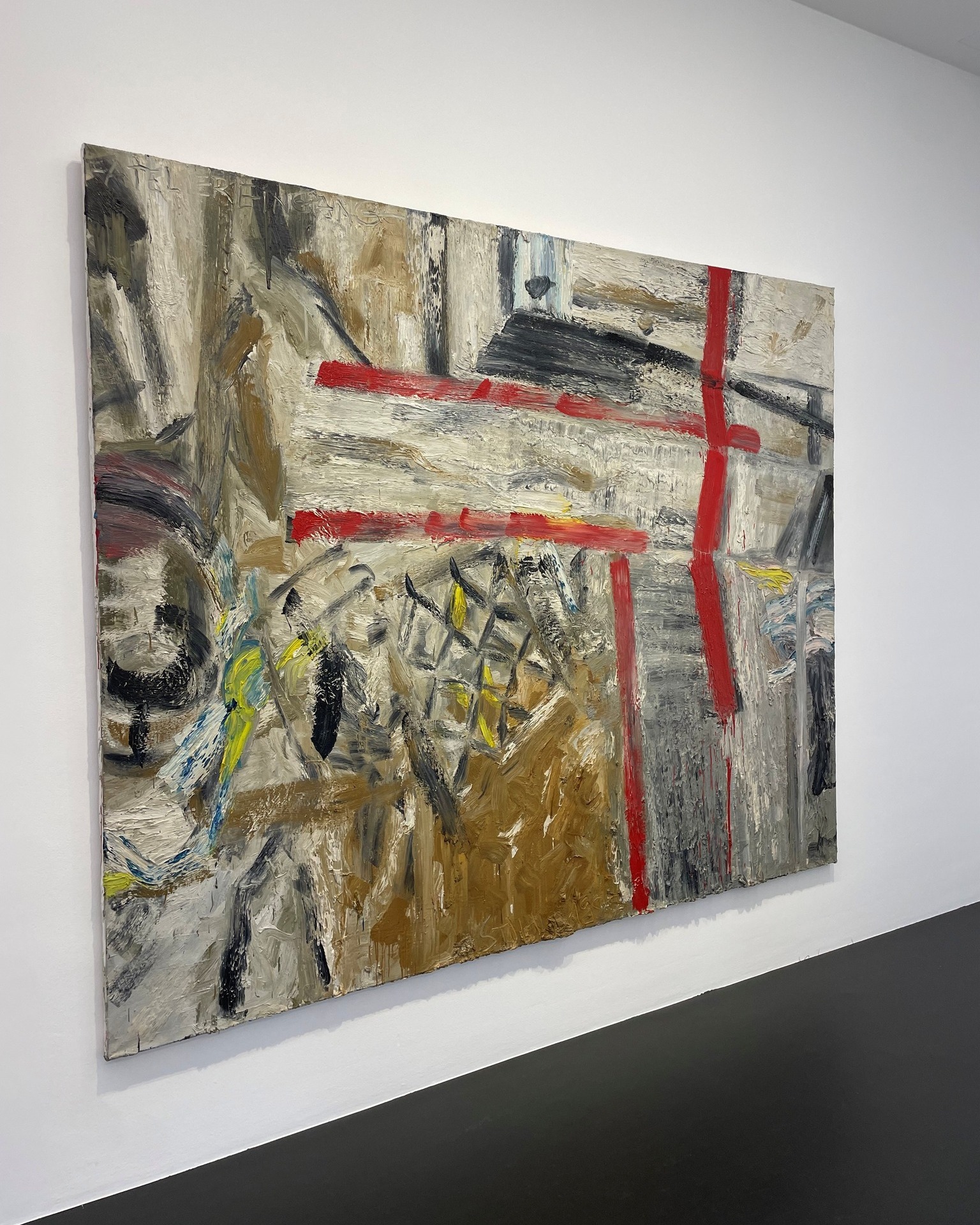 Dieser Alternativtext wurde KI-generiert: Ein abstraktes Gemälde mit dominierenden Grautönen und roten Akzenten hängt an einer weißen Wand. Das Bild zeigt grobe Pinselstriche und unregelmäßige Formen.