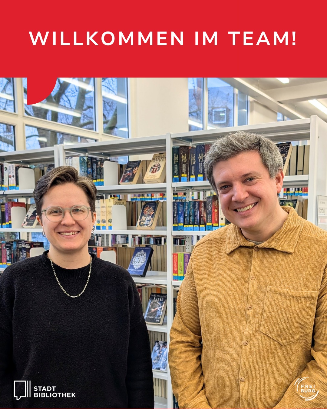 Dieser Alternativtext wurde KI-generiert: Zwei Personen stehen vor Büchern in einem Bibliotheksraum. Im Hintergrund ist durch ein Fenster eine Landschaft mit Bäumen zu sehen.