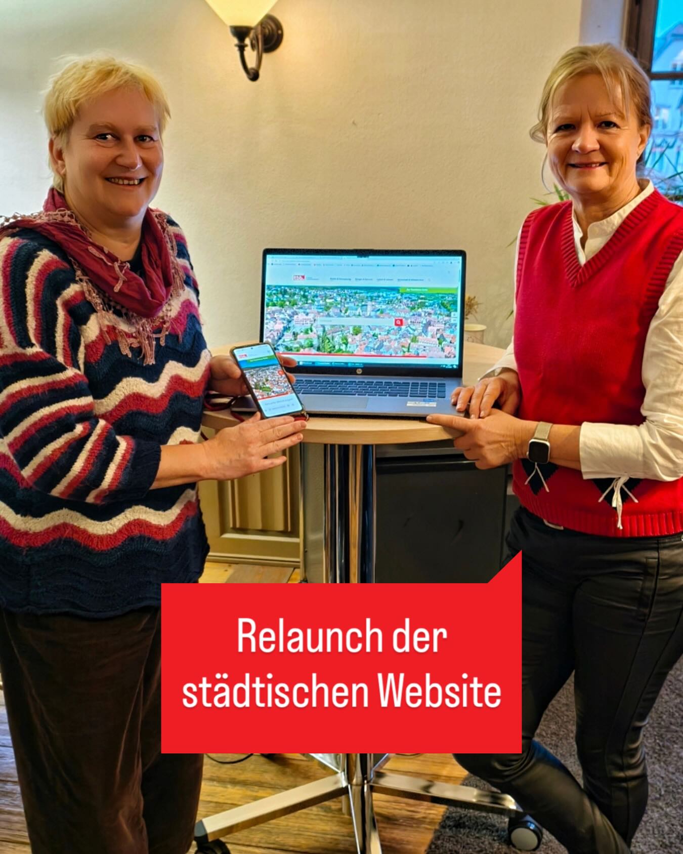 Dieser Alternativtext wurde KI-generiert: Zwei Personen sitzen nebeneinander und halten jeweils ein Mobiltelefon und ein geöffnetes Laptop hoch. Auf dem Laptopbildschirm ist eine Webseite mit einer Stadtansicht zu sehen, ein roter Text im Bild kündigt den Relaunch einer städtischen Webseite an.
