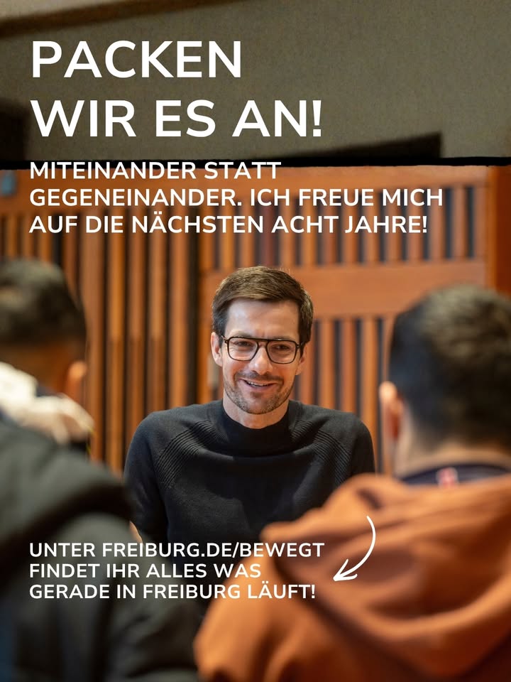 Ein Poster mit dem Text „PACKEN WIR ES AN! MITEINANDER STATT GEGENEINANDER. ICH FREUE MICH AUF DIE NÄCHSTEN ACHT JAHRE!“ oben und der Webadresse „FREIBURG.DE/BEWEGT“ unten. Im Zentrum sitzt eine lächelnde Person mit Brille und dunklem Pullover, während im Vordergrund zwei weitere Personen von hinten zu sehen sind. (KI-Alternativtext)