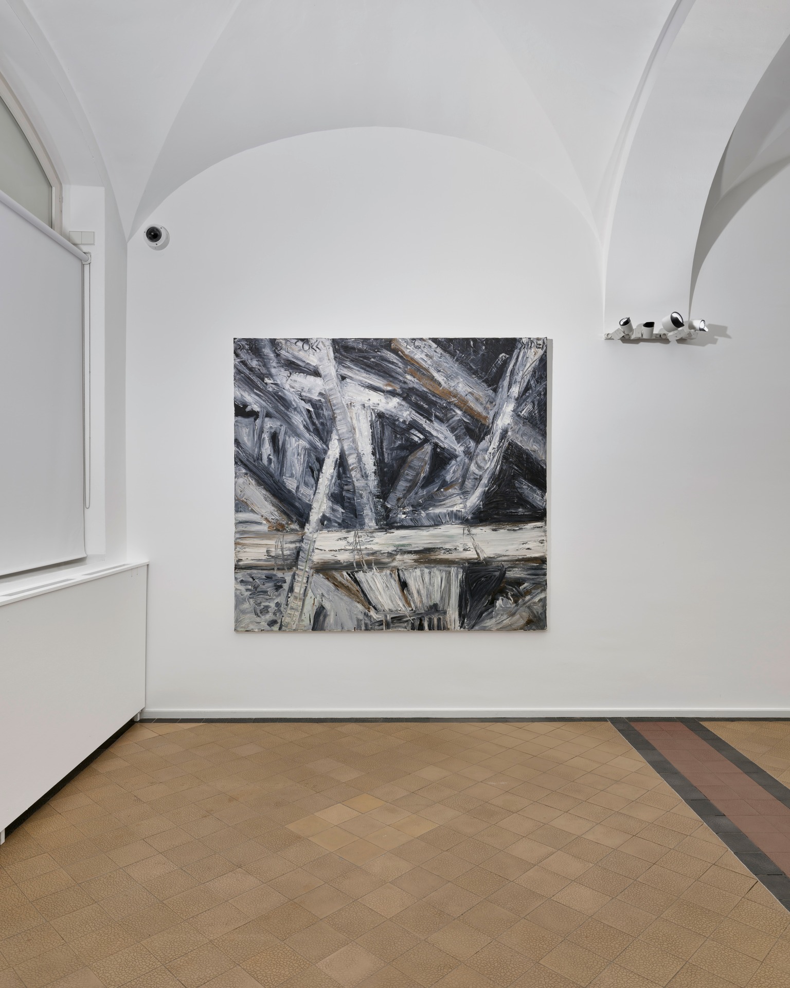 Dieser Alternativtext wurde KI-generiert: Ein abstraktes Gemälde hängt an einer weißen Wand in einem Raum mit gewölbter Decke und Fliesenboden. Das Bild ist überwiegend in Schwarz- und Weißtönen gehalten.