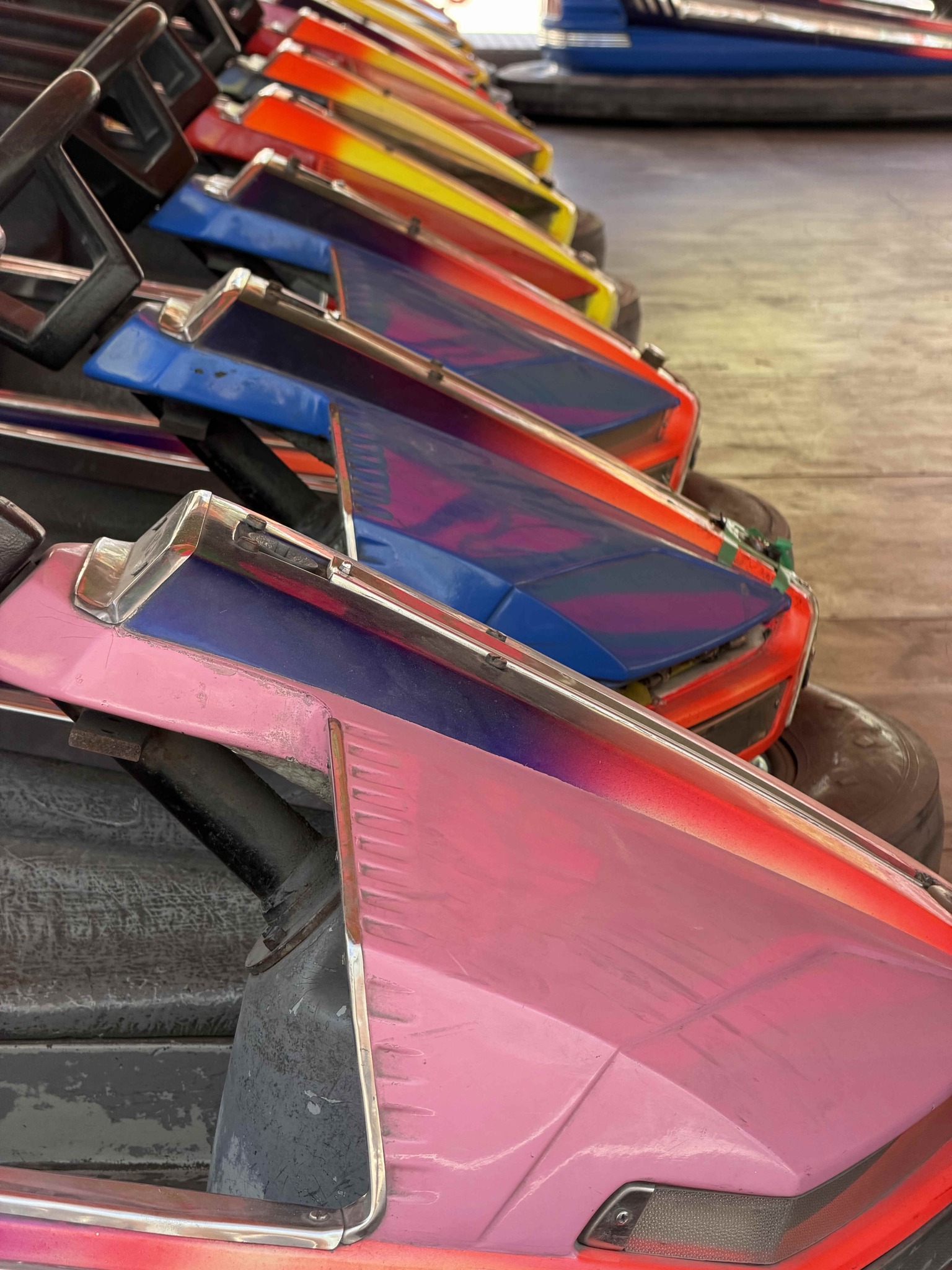 Dieser Alternativtext wurde KI-generiert: Eine Nahaufnahme von mehreren farbenfrohen, ineinander gereihten Fahrzeugen. Die Oberfläche der Fahrzeuge weist lebendige Muster und Farbverläufe auf.