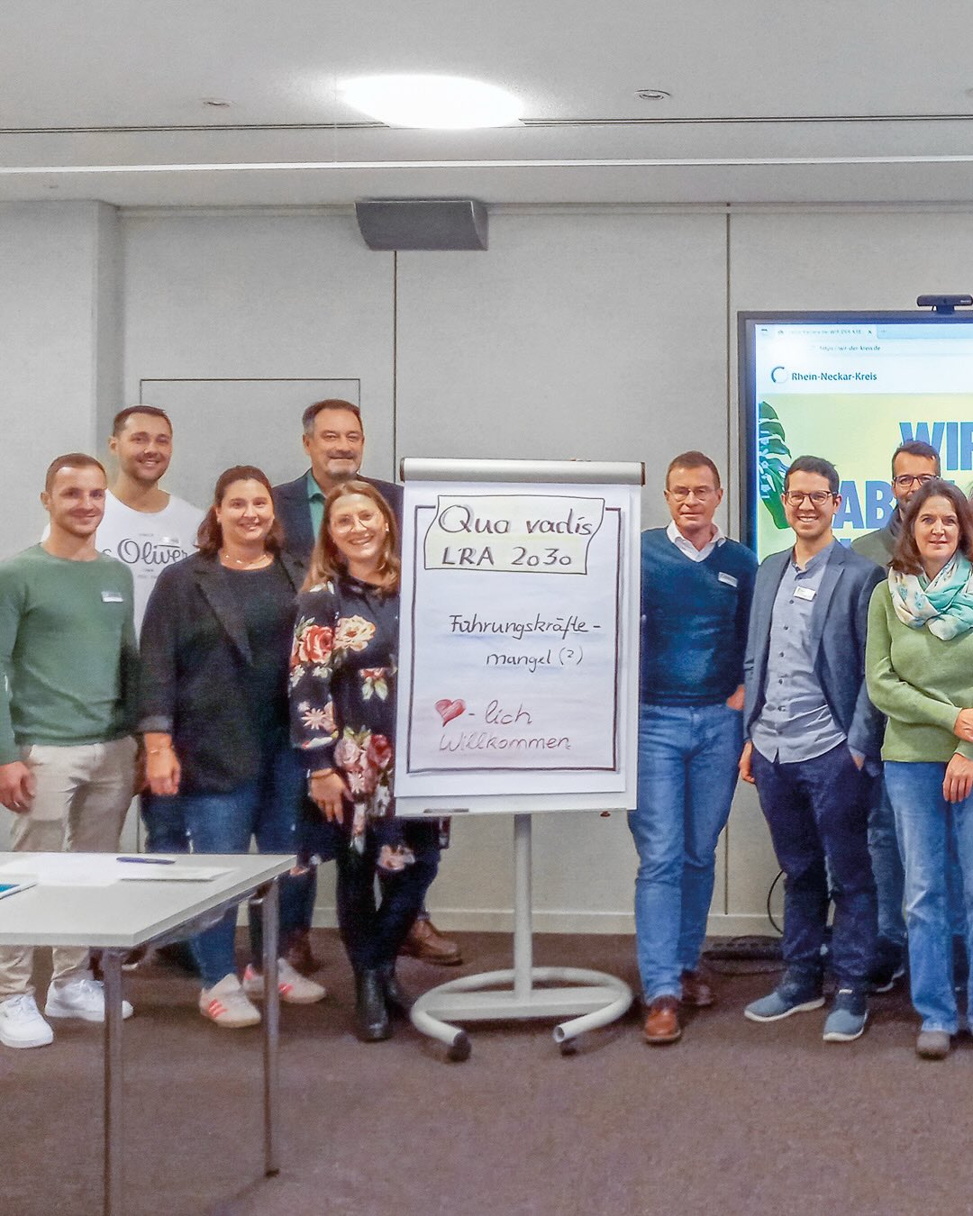 Dieser Alternativtext wurde KI-generiert: Eine Gruppe von Personen steht zusammen vor einer weißen Tafel mit Text und Zeichnungen. Das Bild ist farbig und zeigt eine Innenaufnahme eines Raumes.