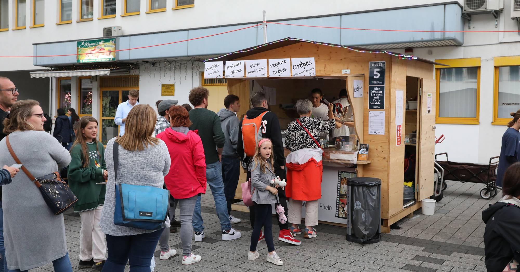 Menschen stehen in einer Schlange vor einem Imbissstand.  Es werden Crêpes und andere Leckereien verkauft.
