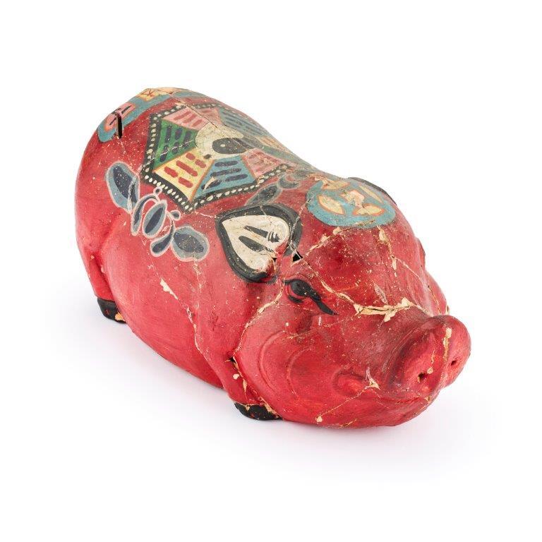 Dieser Alternativtext wurde KI-generiert: Ein rotes, bemaltestes Objekt in Tierform liegt auf einer weißen Oberfläche. Es weist dekorative Elemente und eine unregelmäßige Textur auf.