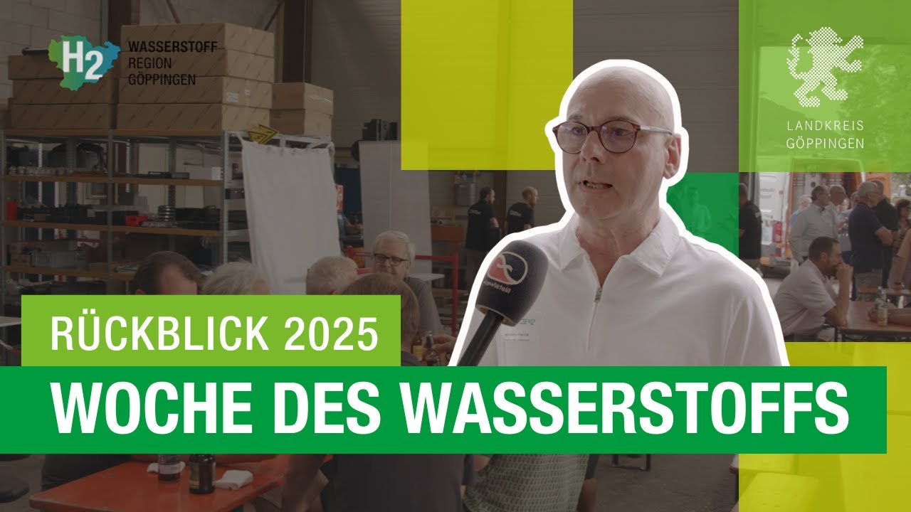 Ein Mann hält ein Mikrofon und spricht in eine Kamera. Im Hintergrund sind Menschen bei einer Veranstaltung zu sehen, mit Text und Logos zu Wasserstofftechnologie.