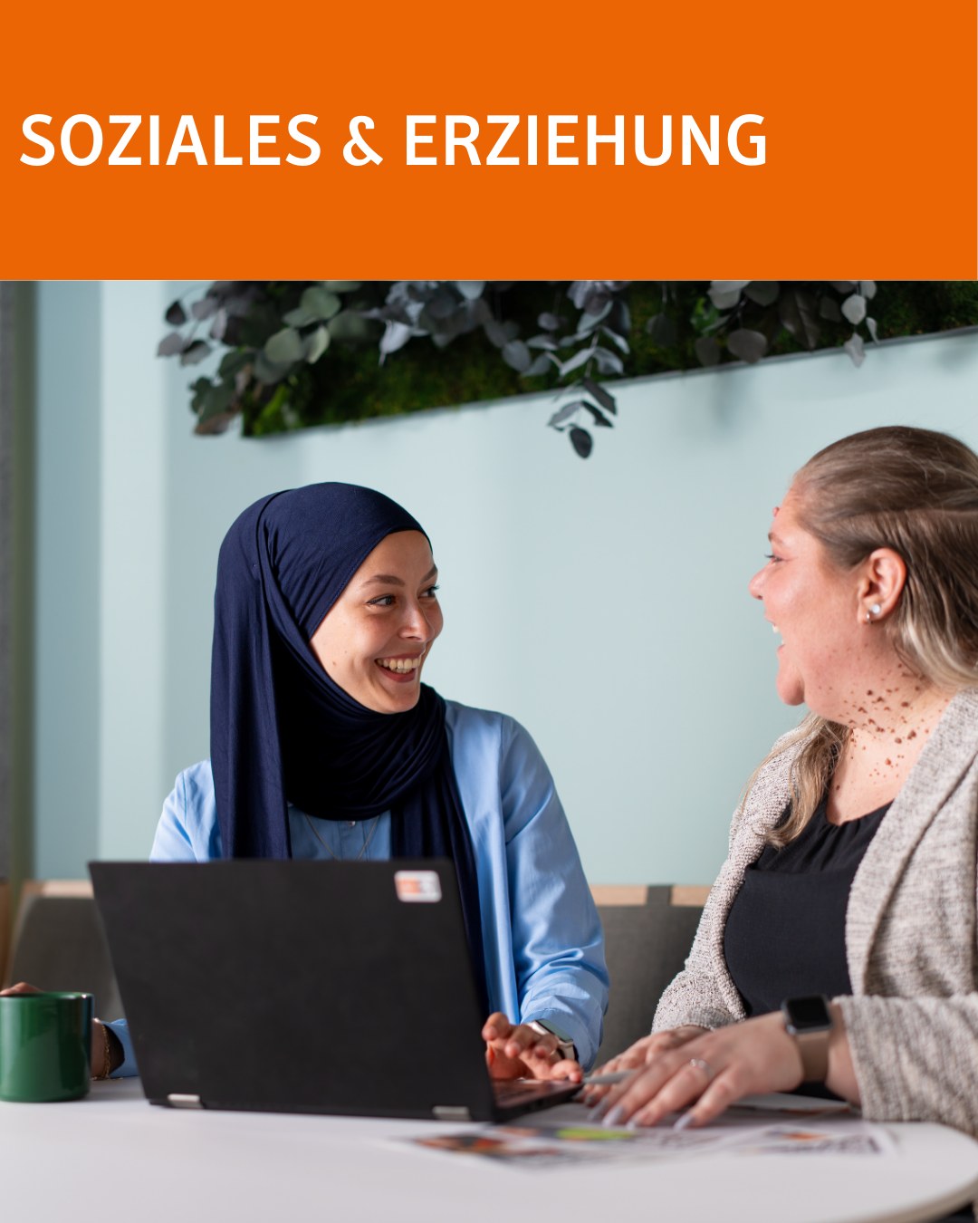 Dieser Alternativtext wurde KI-generiert: Zwei Personen sitzen einander zugewandt und unterhalten sich. Ein Laptop steht zwischen ihnen auf einem Tisch.