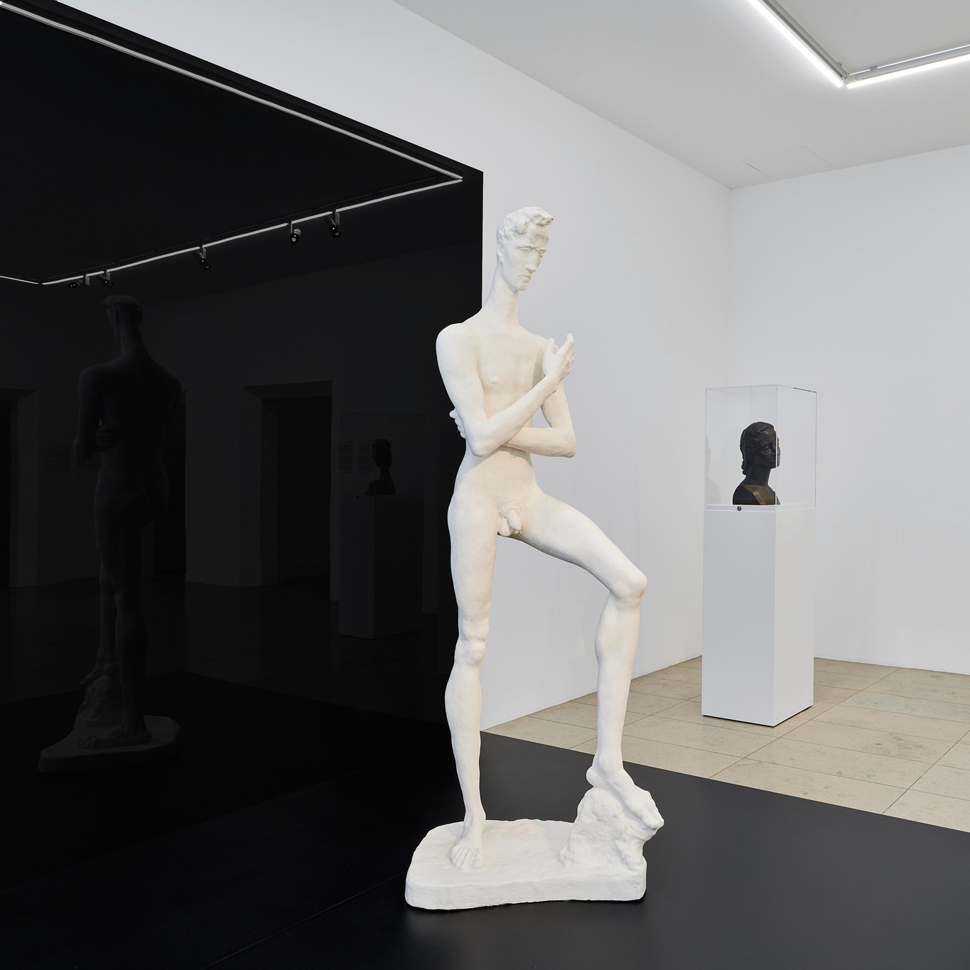 Dieser Alternativtext wurde KI-generiert: Eine helle Ausstellungshalle mit mehreren weißen Skulpturen auf dunklen Sockeln. Die Skulpturen stellen menschliche Formen dar.