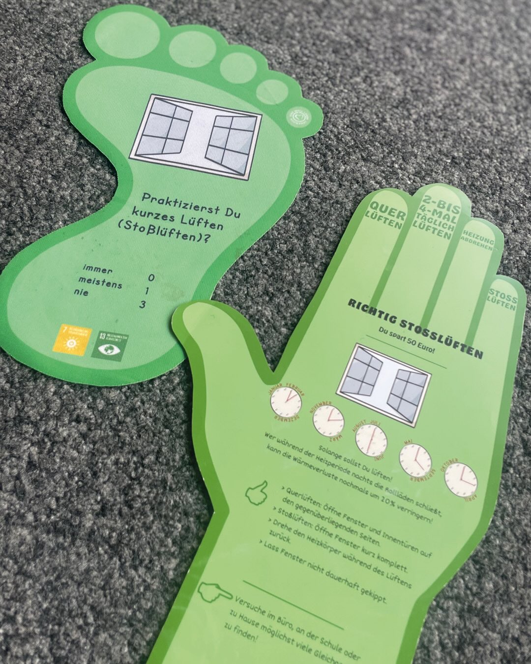 Zwei grüne, fuß- und handförmige Informationskarten zum Stoßlüften: Eine fragt nach der Häufigkeit des Lüftens, die andere erklärt richtiges Stoßlüften mit Tipps und einem Sparhinweis von 50 Euro. Beide zeigen geöffnete Fenster und Symbole für Nachhaltigkeitsziele. (KI-Alternativtext)