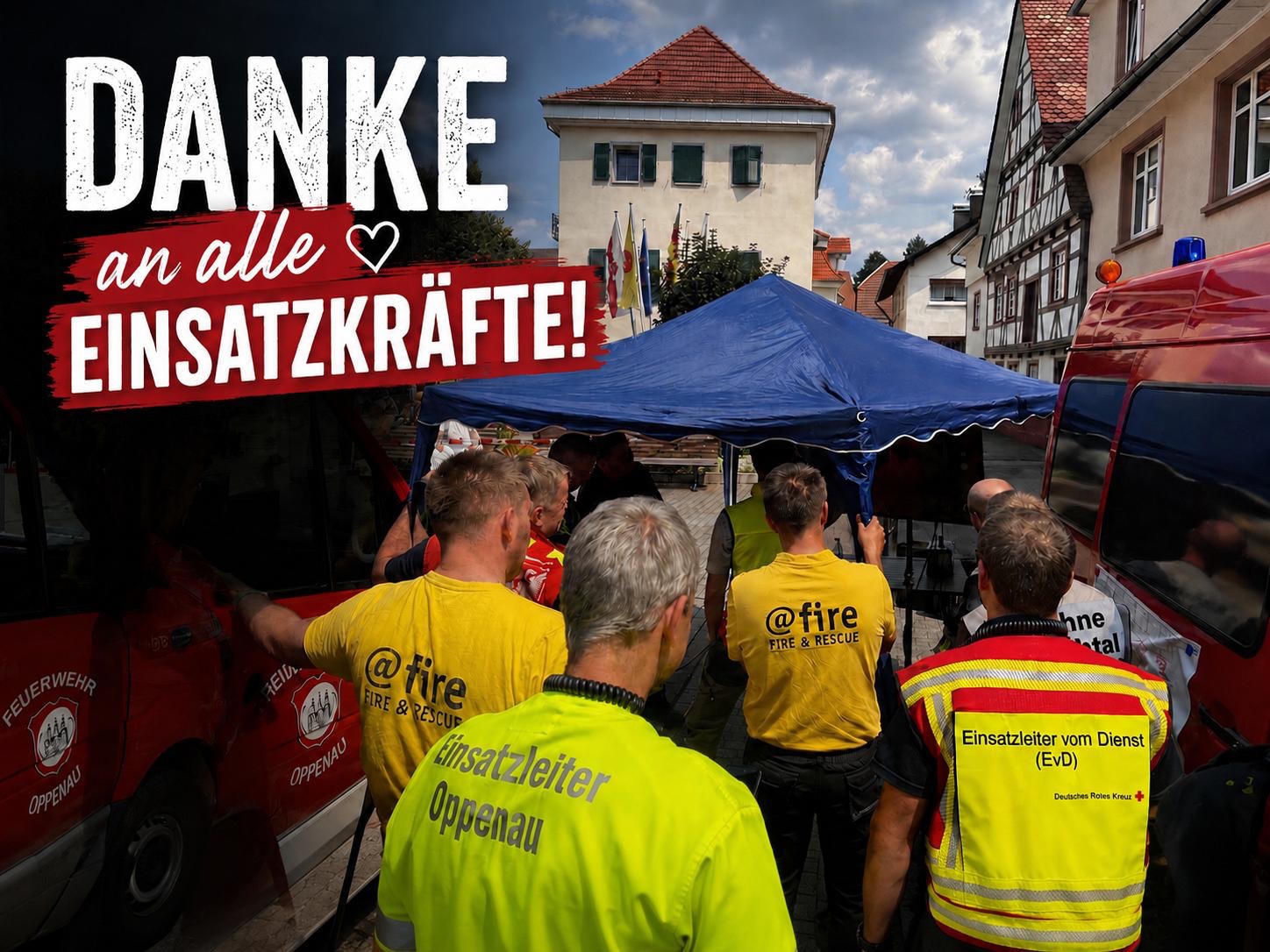 Im oberen linken Bereich steht in großer weißer und roter Schrift „DANKE an alle EINSATZKRÄFTE!“. Mehrere Personen stehen im Vordergrund von hinten in gelben und reflektierenden Westen mit Aufschriften wie „Einsatzleiter Oppenau“ und „Deutsches Rotes Kreuz“. Rote Einsatzfahrzeuge flankieren die Gruppe, im Hintergrund steht ein blaues Zelt vor Gebäuden. (KI-Alternativtext)