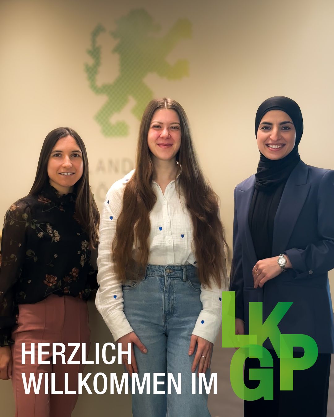 Dieser Alternativtext wurde KI-generiert: Drei Personen lächeln in die Kamera. Im Hintergrund befindet sich ein Banner mit Text und einem stilisierten Löwen.