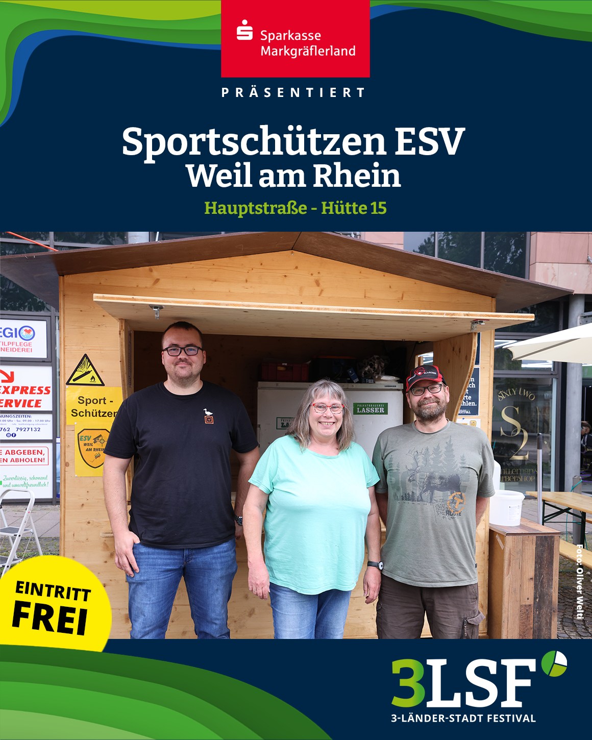 Drei Personen stehen vor einer Holzhütte mit Schildern von „Sportschützen ESV Weil am Rhein“ und „Eintritt frei“. Oben ist das Logo der Sparkasse Markgräflerland, unten das des 3-Länder-Stadt-Festivals. (KI-Alternativtext)